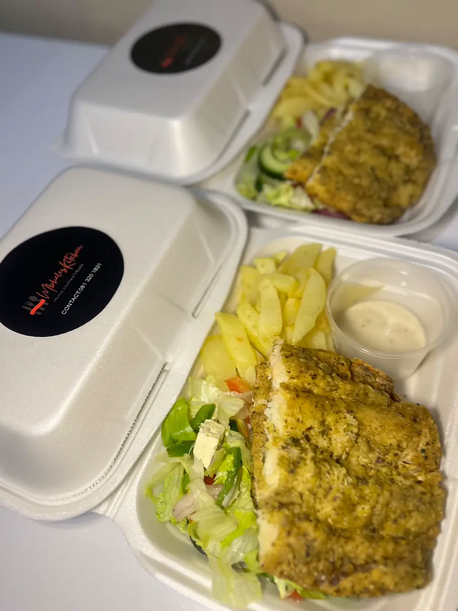 Two takeout meal containers with seasoned grilled chicken, potatoes, salad, and dipping sauce